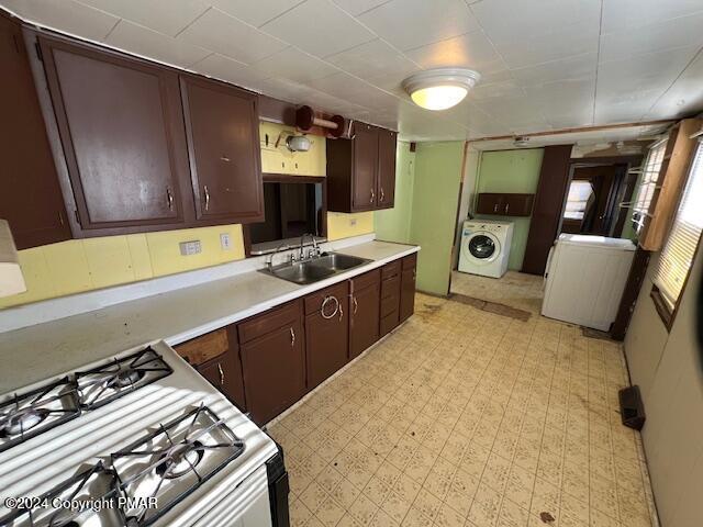 kitchen with light floors, light countertops, a sink, white range with gas cooktop, and washer / dryer