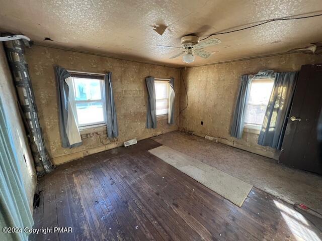 unfurnished room featuring plenty of natural light, wood-type flooring, visible vents, and a ceiling fan