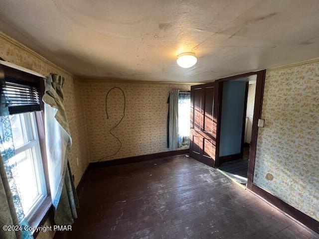 unfurnished room featuring ornamental molding, wood finished floors, baseboards, and wallpapered walls