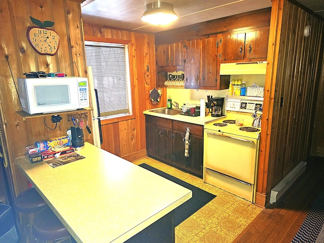 kitchen with under cabinet range hood, a sink, white appliances, wood walls, and light countertops