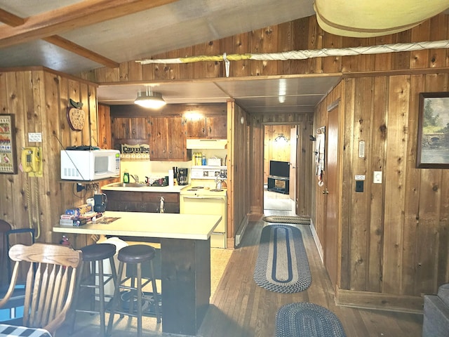 kitchen featuring under cabinet range hood, white appliances, wooden walls, light countertops, and vaulted ceiling with beams