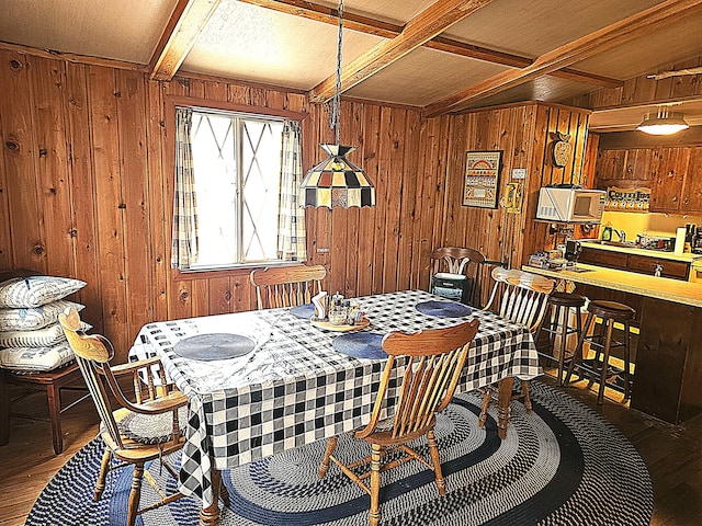 dining room with beam ceiling, wood walls, coffered ceiling, and wood finished floors