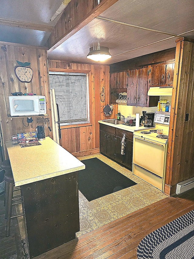 kitchen featuring under cabinet range hood, wood walls, light countertops, white appliances, and a sink