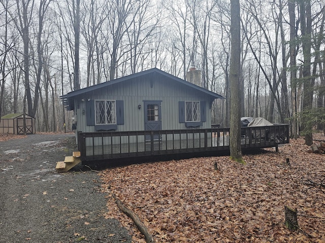 view of front of house with a deck, driveway, a shed, an outdoor structure, and a chimney