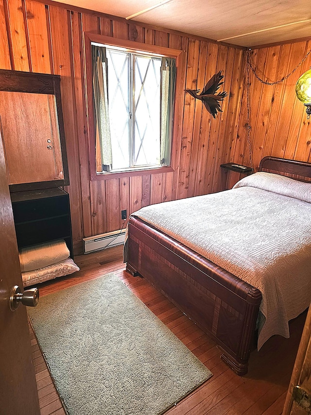 bedroom with wood-type flooring, wood walls, and baseboard heating