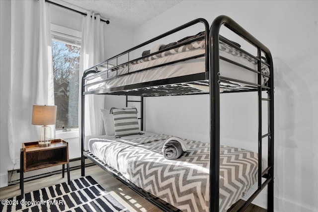 bedroom featuring a textured ceiling, baseboard heating, and wood finished floors