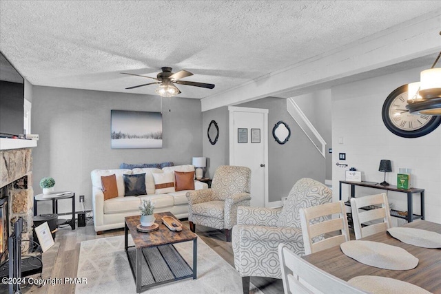 living area with light wood-type flooring, a textured ceiling, a ceiling fan, and a stone fireplace