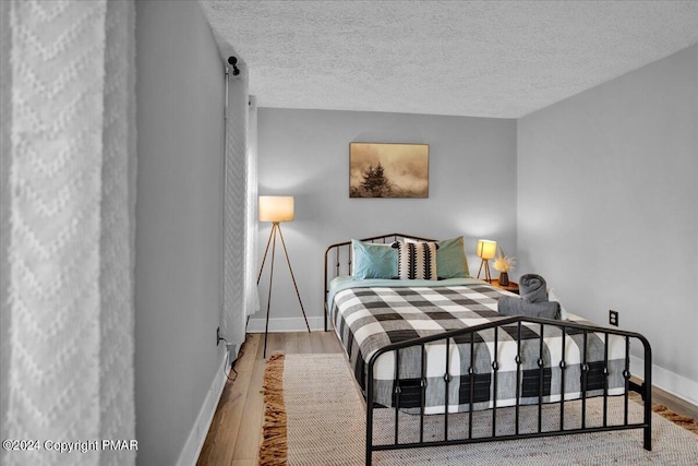 bedroom featuring a textured ceiling, baseboards, and wood finished floors