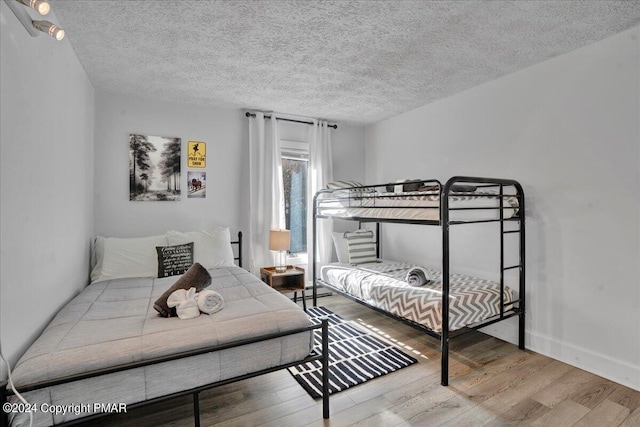 bedroom with a textured ceiling, baseboards, and wood finished floors