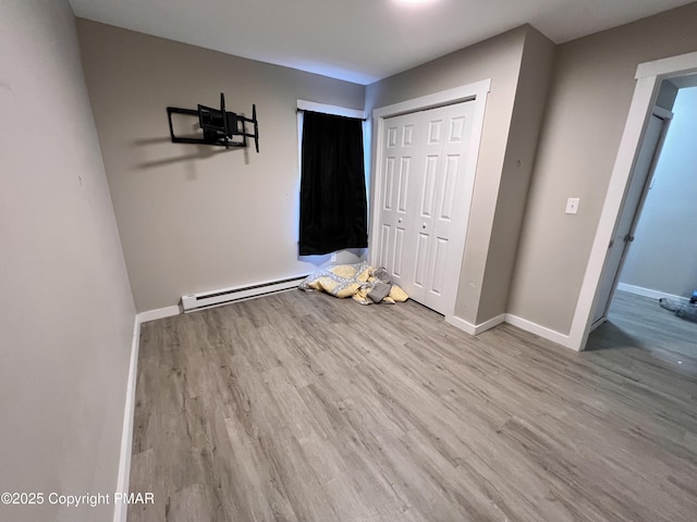 unfurnished bedroom featuring a closet, wood finished floors, baseboards, and a baseboard radiator