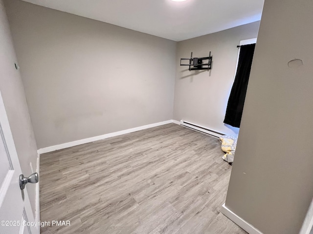 empty room with a baseboard heating unit, baseboards, and wood finished floors