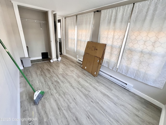 unfurnished bedroom featuring a closet, a baseboard heating unit, baseboards, and wood finished floors