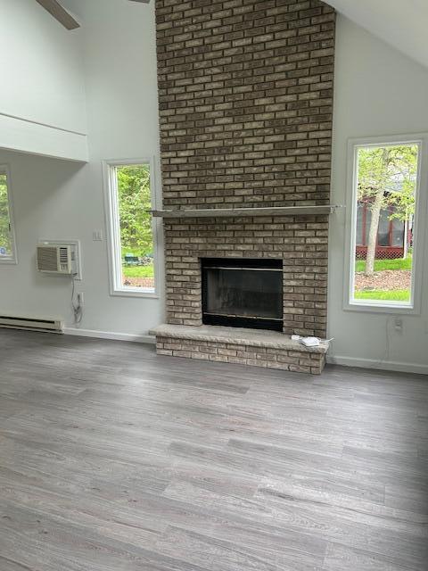 124 Segatti Cir, Bushkill, PA 18324 - unfurnished living room with high vaulted ceiling, a wall mounted AC, a brick fireplace, wood finished floors, and baseboards