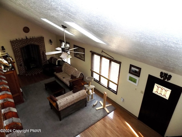 living room featuring wood-type flooring, vaulted ceiling with skylight, a textured ceiling, and a fireplace