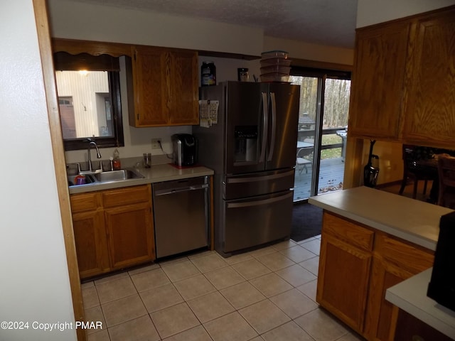 kitchen with light countertops, refrigerator with ice dispenser, stainless steel dishwasher, brown cabinetry, and a sink