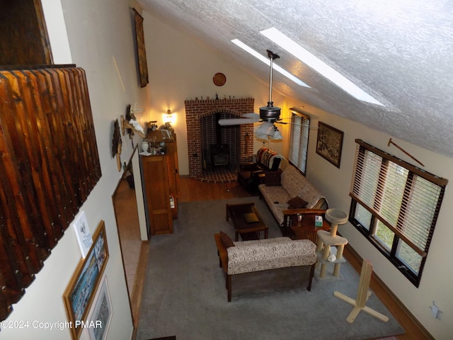 living room with ceiling fan, vaulted ceiling with skylight, a textured ceiling, and a wood stove