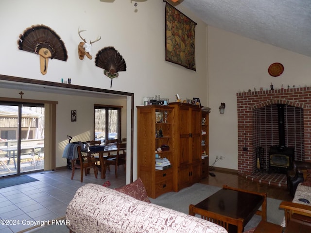 living room with a wood stove, a textured ceiling, tile patterned floors, and high vaulted ceiling