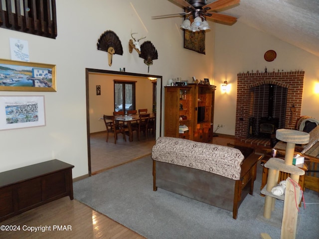 living room with wood-type flooring, high vaulted ceiling, ceiling fan, and a wood stove