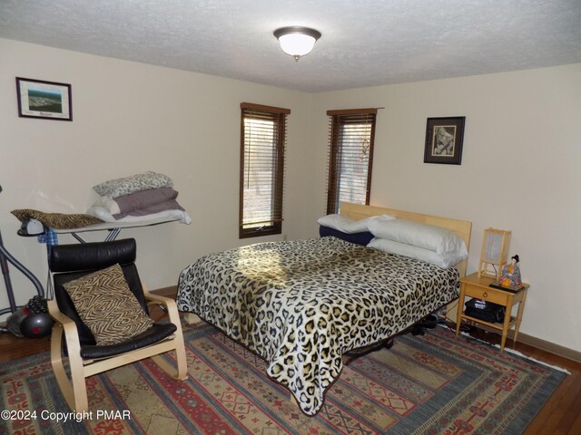 bedroom featuring a textured ceiling, baseboards, and wood finished floors