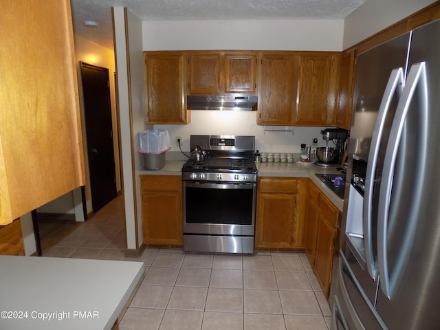 kitchen featuring light tile patterned flooring, light countertops, under cabinet range hood, appliances with stainless steel finishes, and brown cabinets