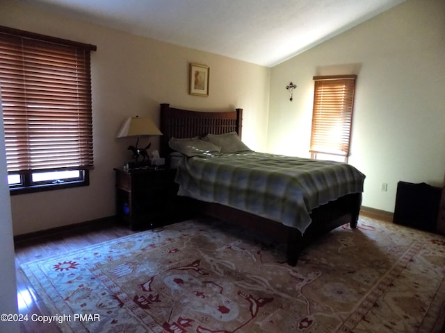 bedroom featuring multiple windows, lofted ceiling, baseboards, and wood finished floors