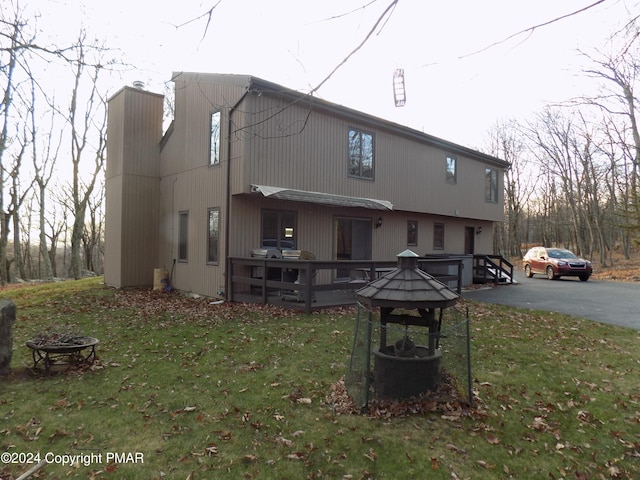 back of property featuring a wooden deck, a yard, a chimney, and an outdoor fire pit