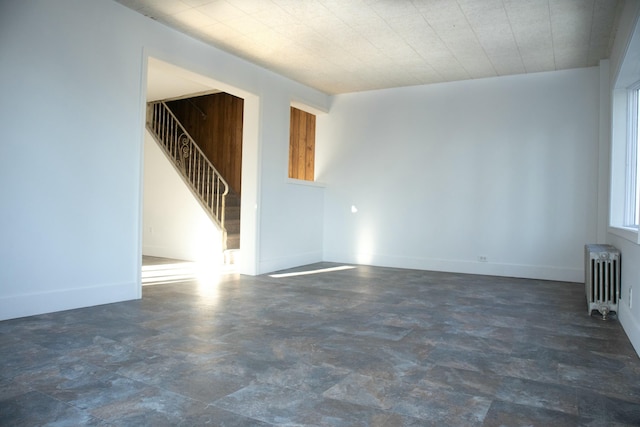 unfurnished living room featuring radiator, baseboards, and stairway