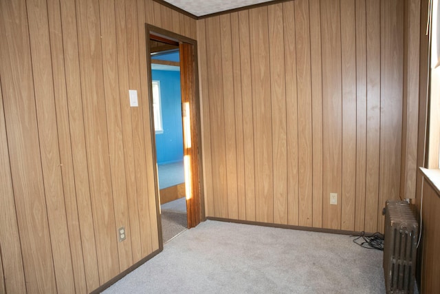 carpeted empty room with radiator heating unit and wooden walls