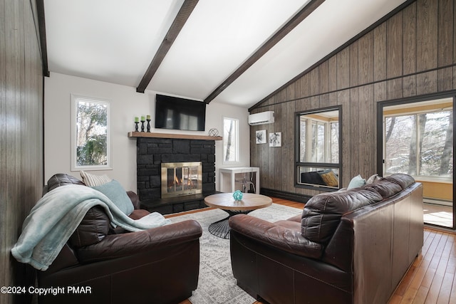 living area featuring vaulted ceiling with beams, an AC wall unit, light wood-type flooring, and a wealth of natural light