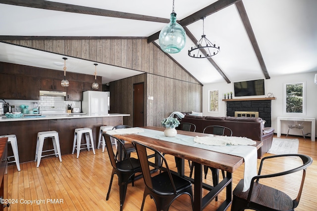 dining room with vaulted ceiling with beams, light wood-style floors, a fireplace, and a chandelier