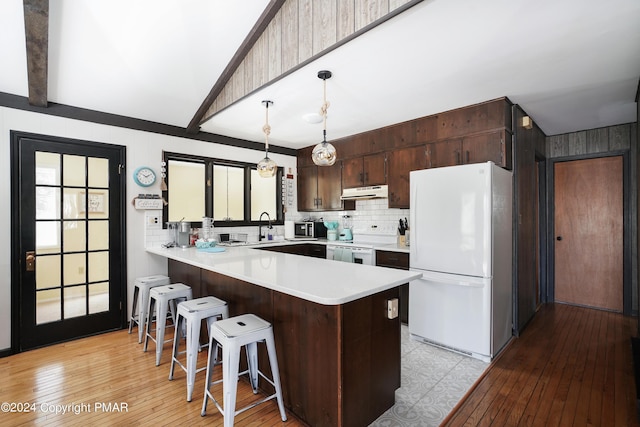 kitchen featuring under cabinet range hood, a peninsula, white appliances, a kitchen breakfast bar, and light countertops