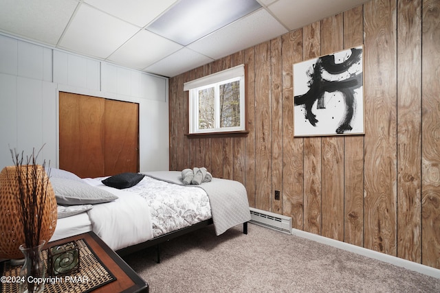 carpeted bedroom featuring wooden walls, a closet, baseboard heating, and a drop ceiling