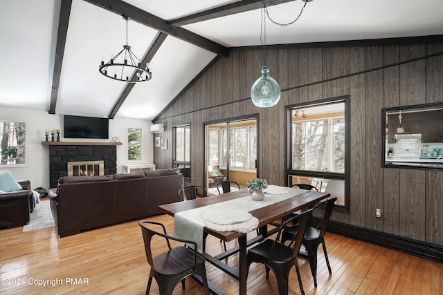 dining area featuring plenty of natural light, light wood-style flooring, beam ceiling, and a stone fireplace