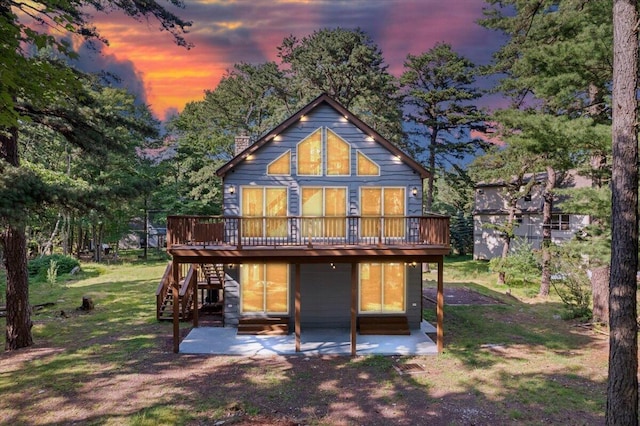 back of property at dusk with stairs, a patio, a deck, and a lawn