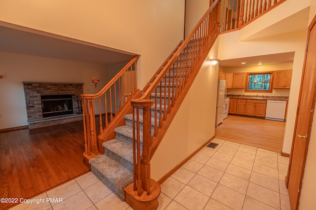 staircase with tile patterned flooring, a brick fireplace, a high ceiling, and sink