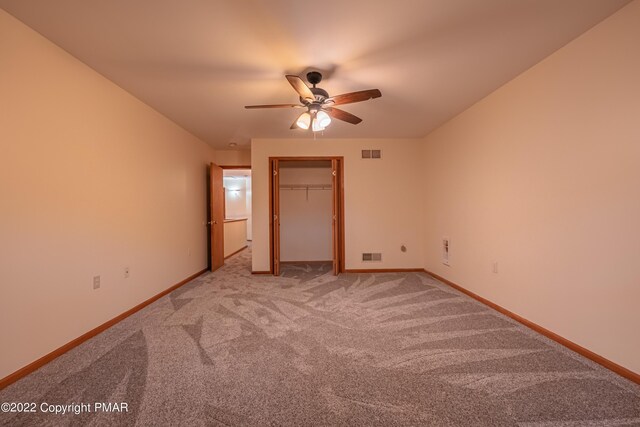 unfurnished bedroom with a walk in closet, carpet floors, a closet, and ceiling fan