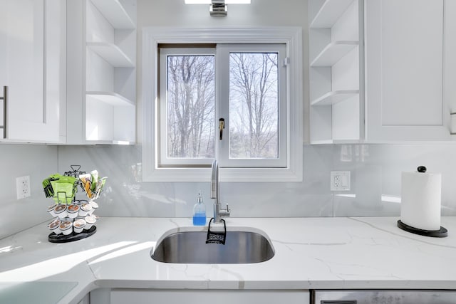 kitchen with white cabinets, light stone counters, open shelves, dishwashing machine, and a sink
