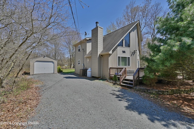 view of property exterior featuring a deck, gravel driveway, an outdoor structure, a garage, and a chimney