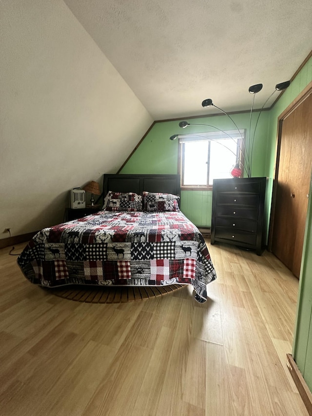 bedroom with vaulted ceiling, wood finished floors, and a textured ceiling