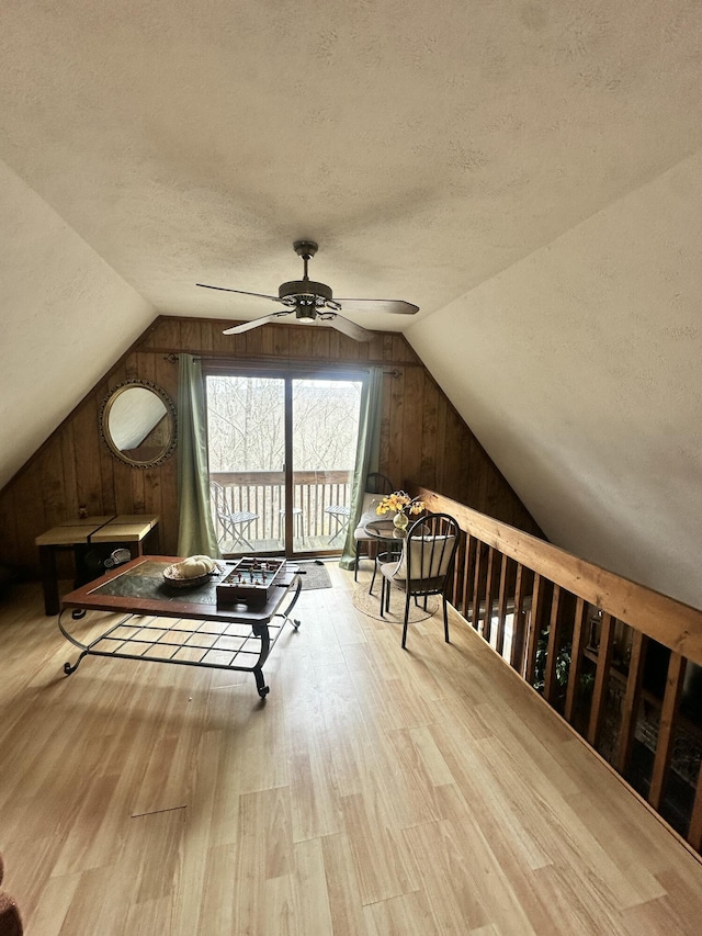 bonus room with a textured ceiling, wood walls, a ceiling fan, and vaulted ceiling