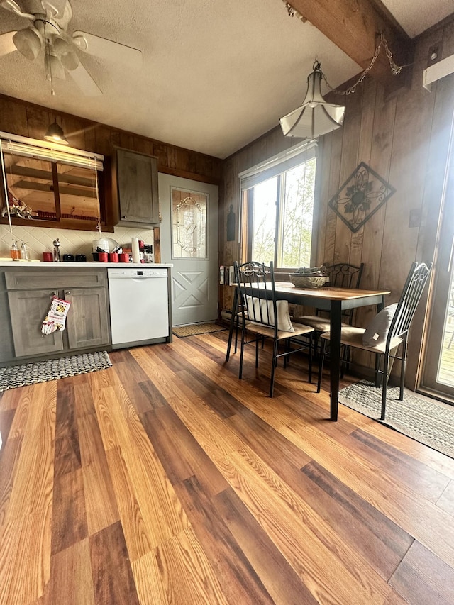 dining room with a ceiling fan, light wood-style floors, a textured ceiling, beamed ceiling, and wood walls