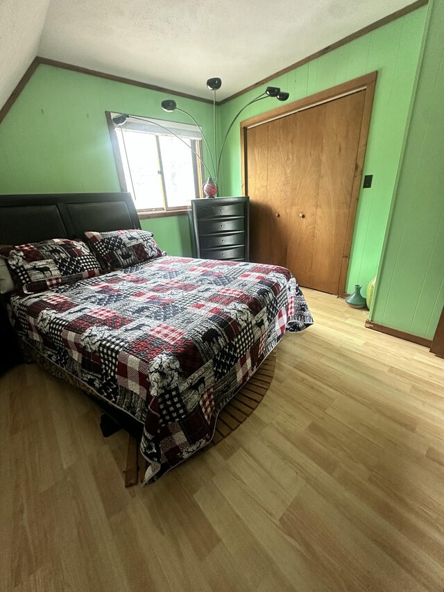 bedroom featuring a closet, a textured ceiling, light wood finished floors, and lofted ceiling