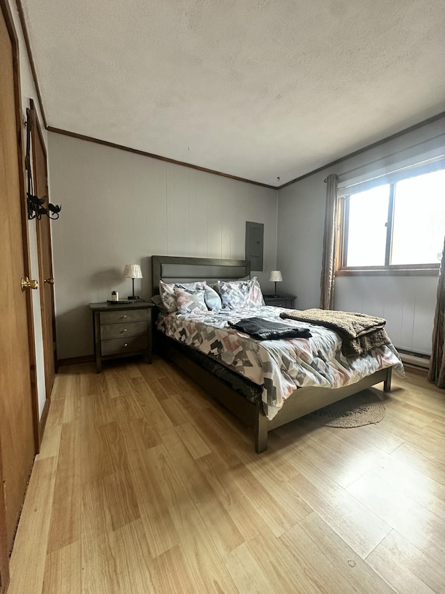 bedroom featuring electric panel, light wood-style flooring, a textured ceiling, and ornamental molding