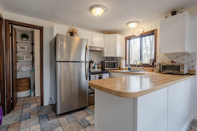 kitchen featuring stainless steel appliances, a sink, a peninsula, tasteful backsplash, and white cabinets