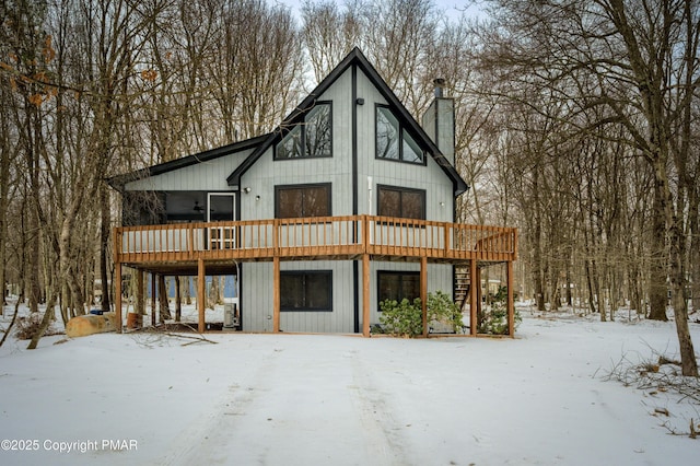 snow covered rear of property with a chimney, a wooden deck, and stairs