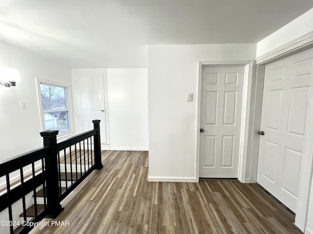 corridor with baseboards, dark wood-type flooring, and an upstairs landing