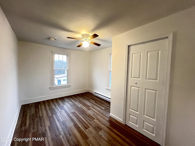 unfurnished bedroom with baseboards, a baseboard heating unit, dark wood finished floors, and a ceiling fan