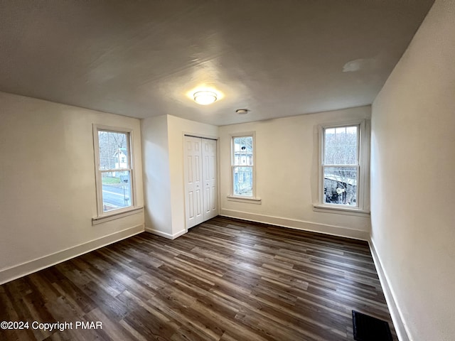 unfurnished bedroom featuring dark wood-type flooring, multiple windows, and baseboards