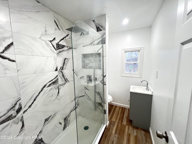 full bath featuring toilet, wood finished floors, vanity, baseboards, and a marble finish shower