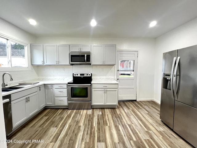 kitchen featuring recessed lighting, stainless steel appliances, a sink, light wood-style floors, and tasteful backsplash